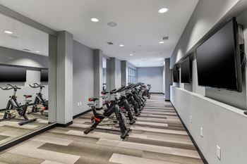 A room with a row of exercise bikes and a television on the wall.